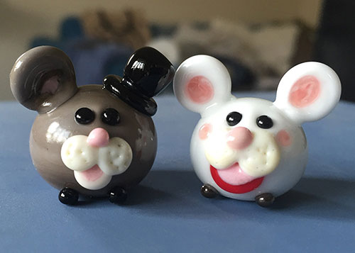 Two glass mice with faces and hats, made using flamework techniques.