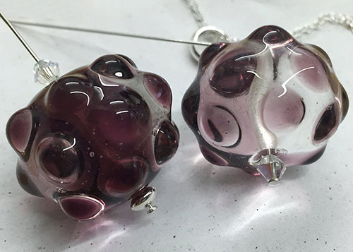 Two clear glass beads made with transparent glass and raised purple bumps on a chain.
